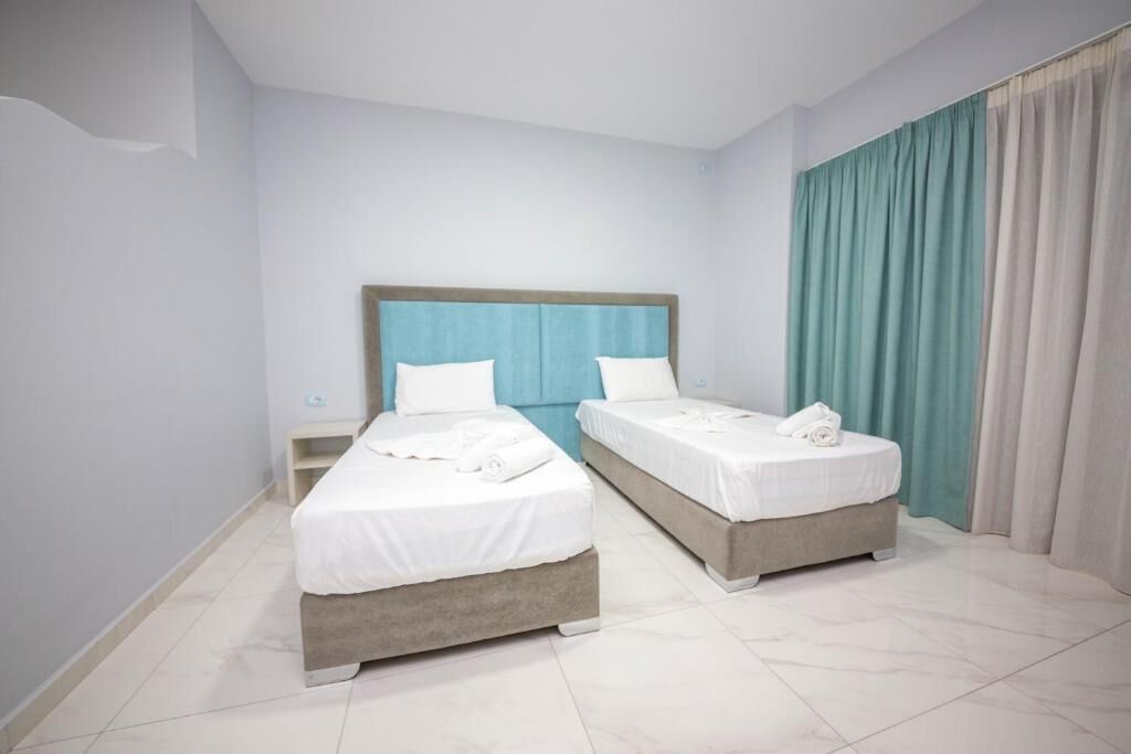 A hotel room with two beds, a wooden headboard, white bedding, and a view of the sea through curtains.