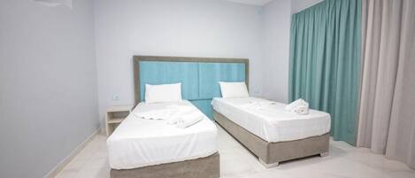 A hotel room with two beds, a wooden headboard, white bedding, and a view of the sea through curtains.