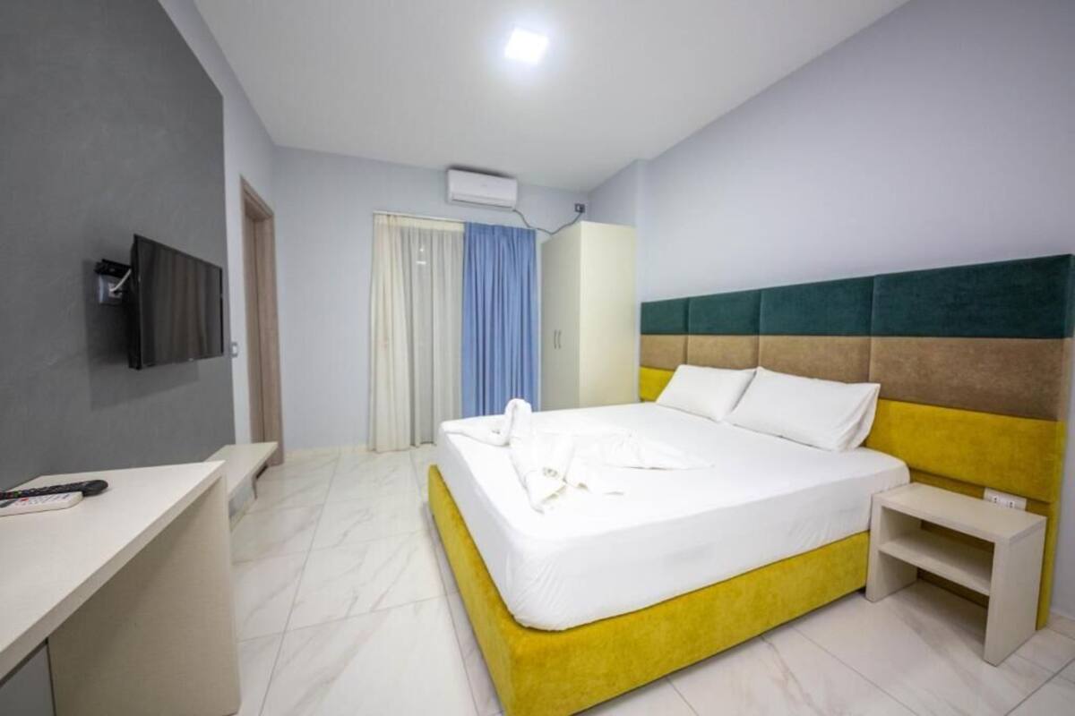 Una habitaci ón de hotel con cama, escritorio, televisor y ventana con cortinas.