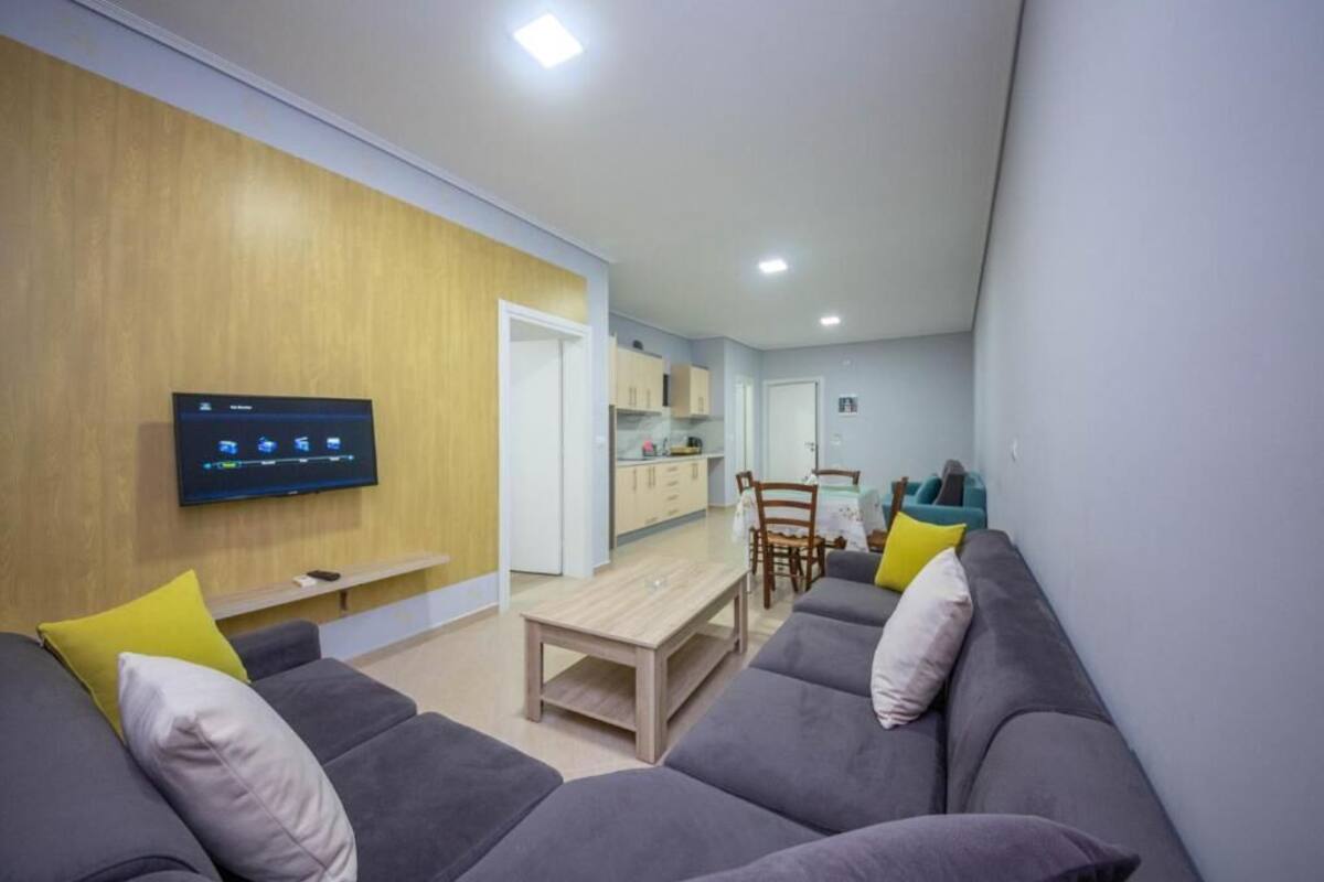 Una sala de estar moderna con un sofá gris, un revestimiento de pared de madera, un televisor de pantalla plana y una zona de comedor con mesa y sillas.