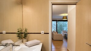 A modern bathroom with a large sink, mirror, and potted plant.