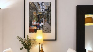 A dining area with a table, chairs, a framed picture, a lamp, and a vase with flowers.