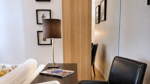 A modern room with a dark wooden desk, a black leather chair, a white sofa, and framed artwork on the wall.