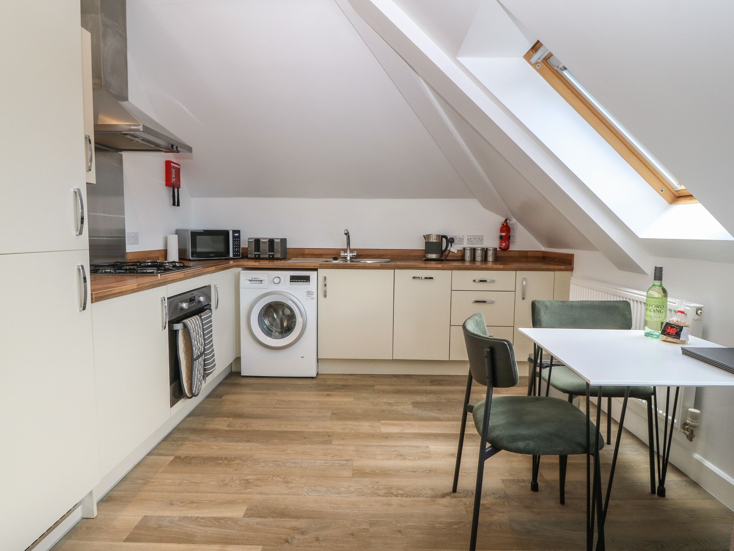Een kleine keuken met een wasmachine, magnetron en een eethoek met een tafel en stoelen.