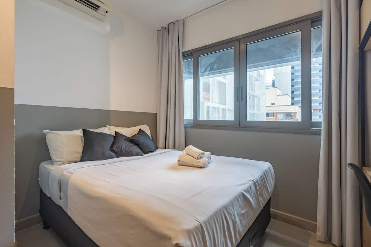 A hotel room with a bed, a window with curtains, and a view of buildings outside.