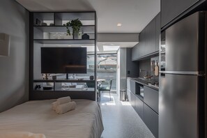 A modern hotel room with a bed, a TV, a kitchen area, and a view of the outside. - 360 VN Oscar Freire by Housi (São Paulo)