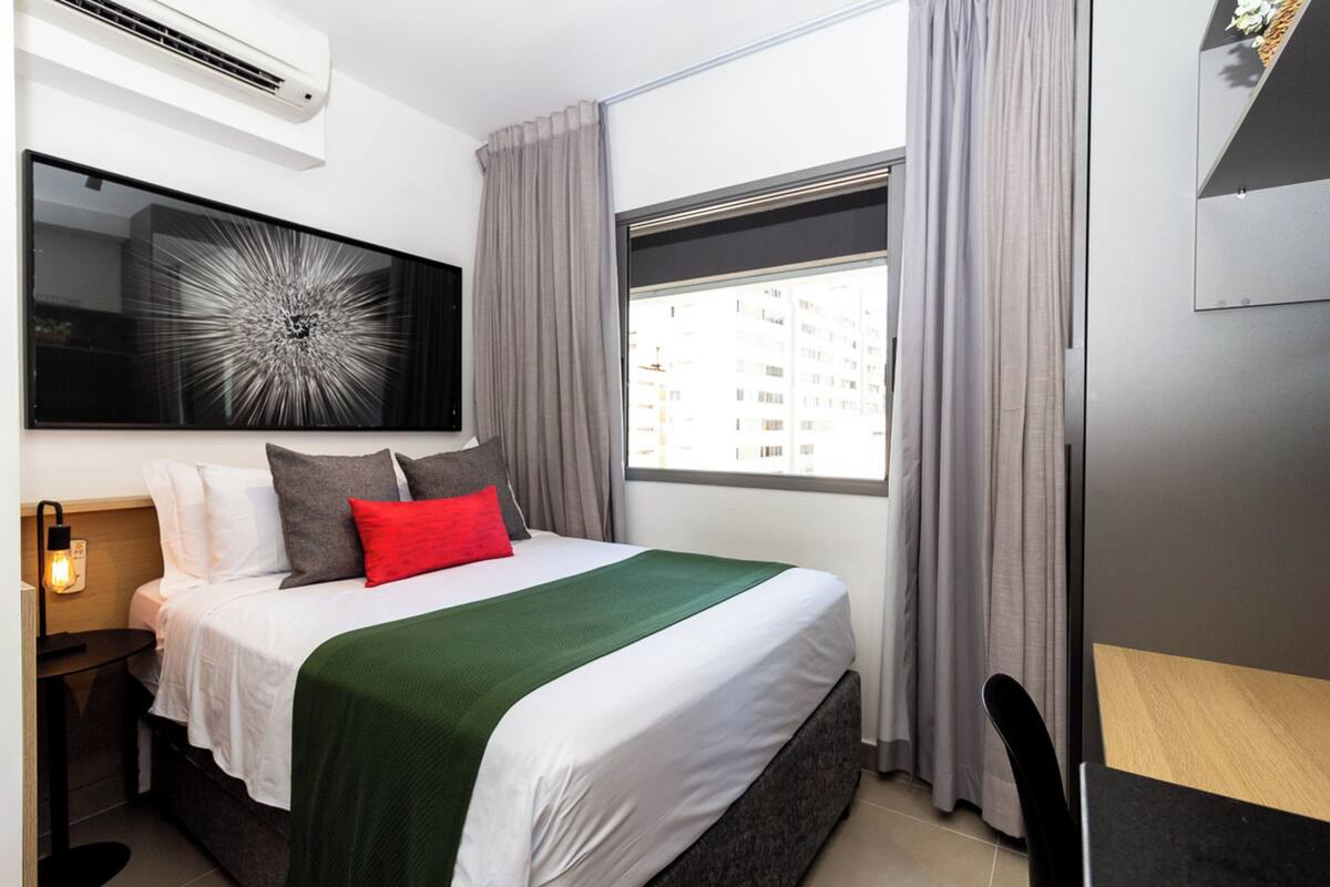 A modern hotel room with a large bed, a flat-screen TV, and a window with curtains.
