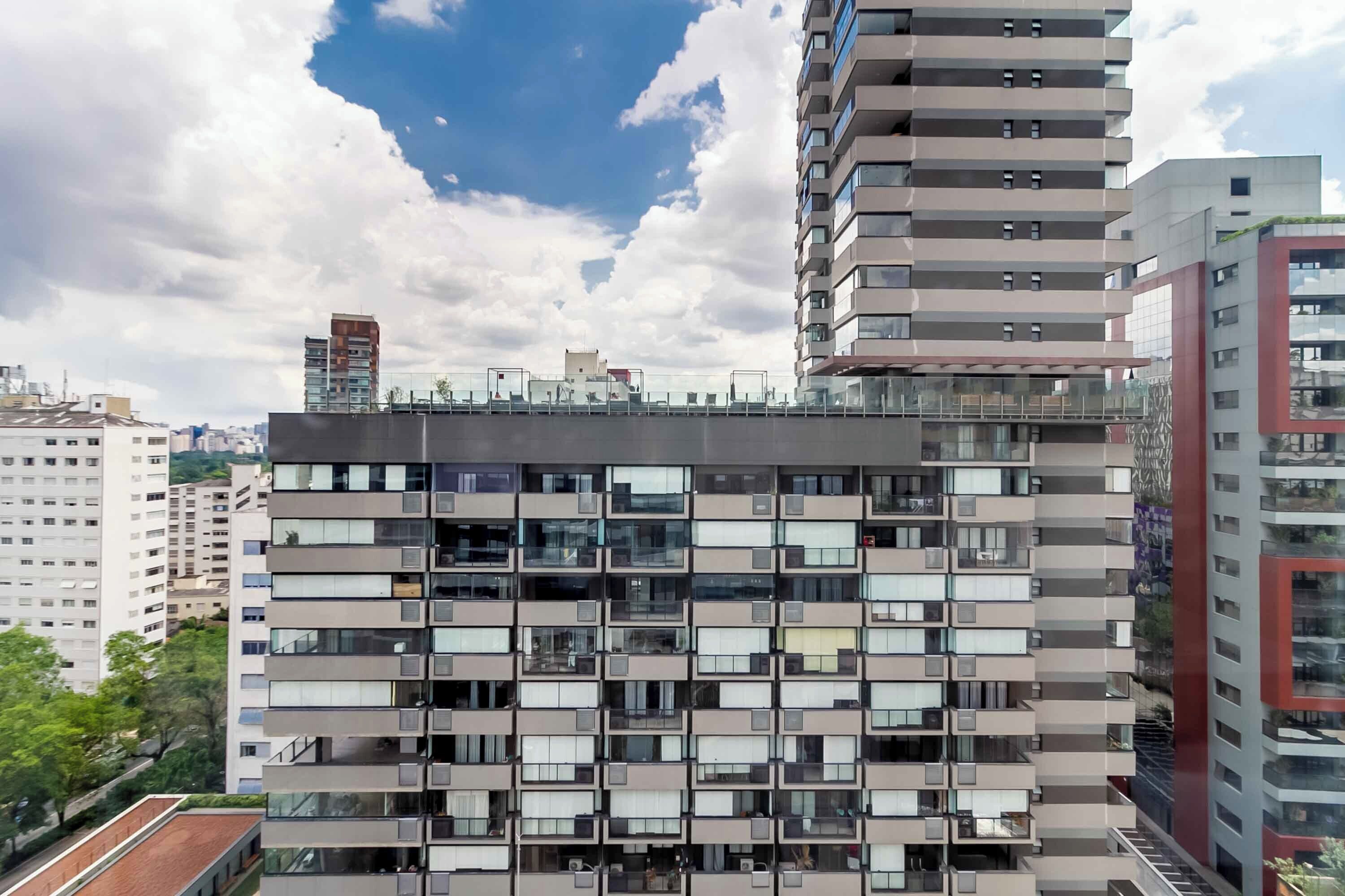 Un edificio moderno de varios pisos con fachada enrejada, múltiples balcones y una terraza en la azotea.