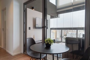 A modern room with a round table, two chairs, a potted plant, and a large window offering a city view. - 360 VN Oscar Freire by Housi (São Paulo)