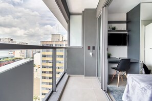 A modern balcony with a city view, a small desk with a chair, and a TV mounted on the wall.