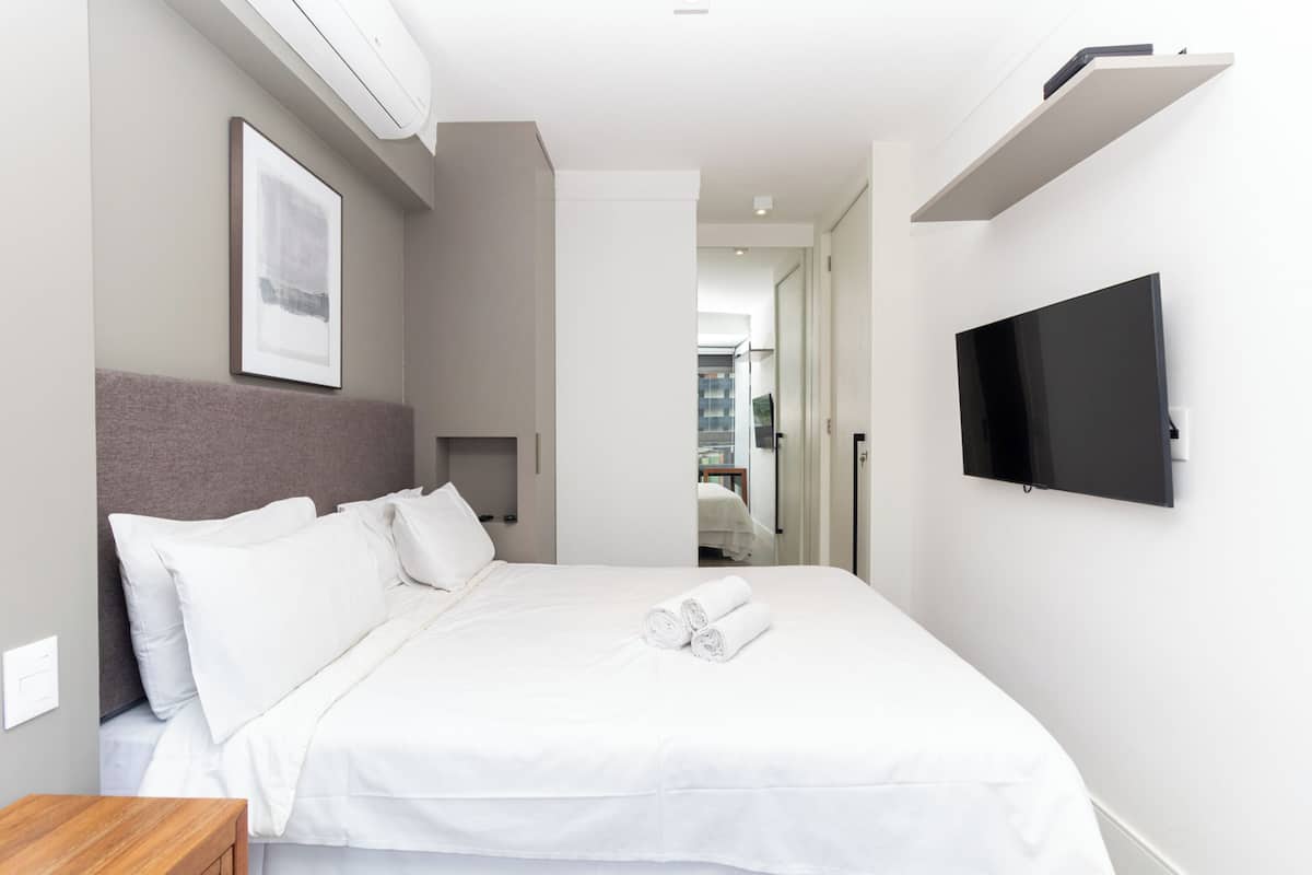 A modern hotel room with a large bed, a flat-screen TV mounted on the wall, and a framed picture above the bed.