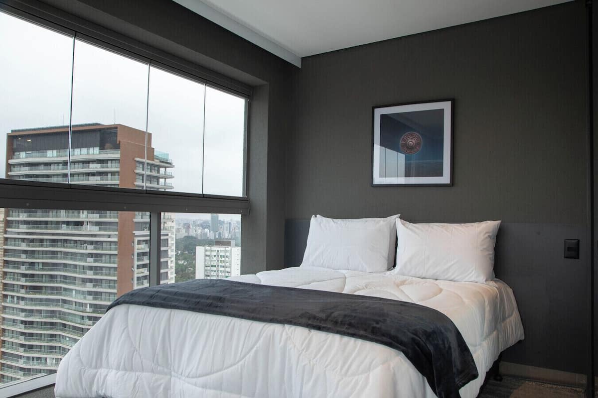 A modern bedroom with a large window, a bed with white bedding, and a framed picture on the wall.