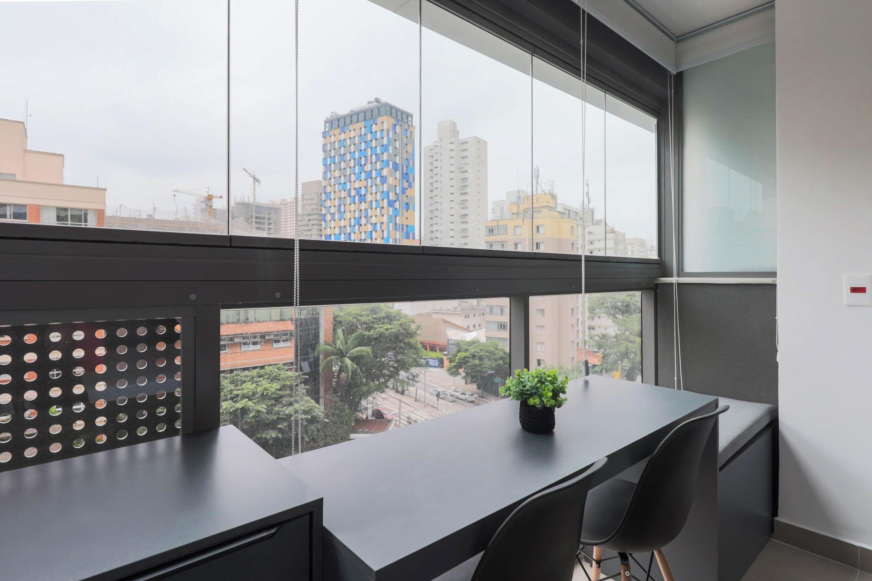 A modern office space with a large window, a desk, two chairs, and a potted plant.