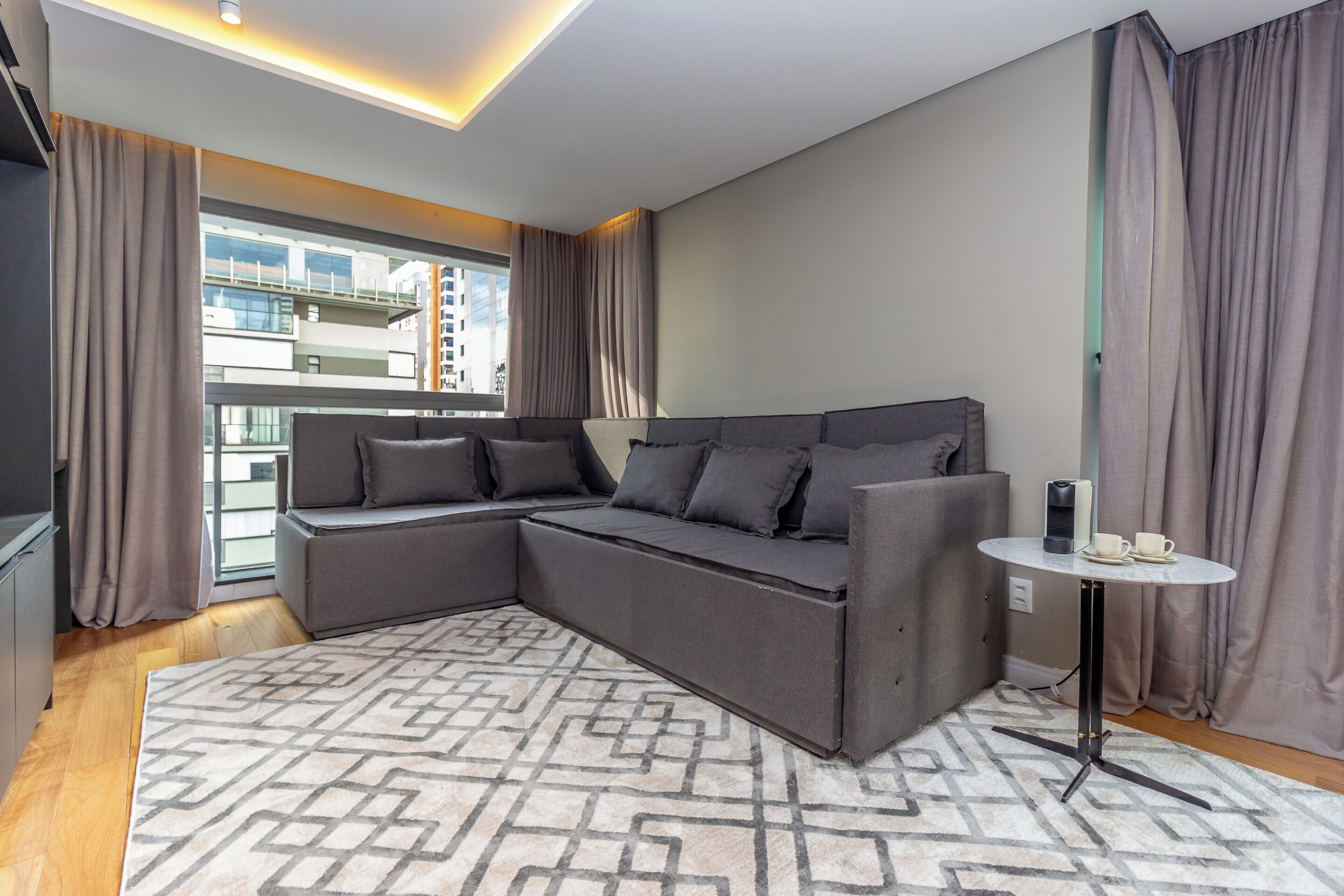 A modern living room with a sectional sofa, a patterned rug, and a small round table with a coffee maker.