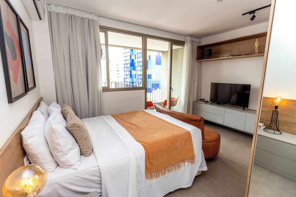 Ein modernes Hotelzimmer mit einem großen Bett, einem Fernseher, einer Holzkammer und einem Balkon mit Blick auf ein blaues Gebäude.
