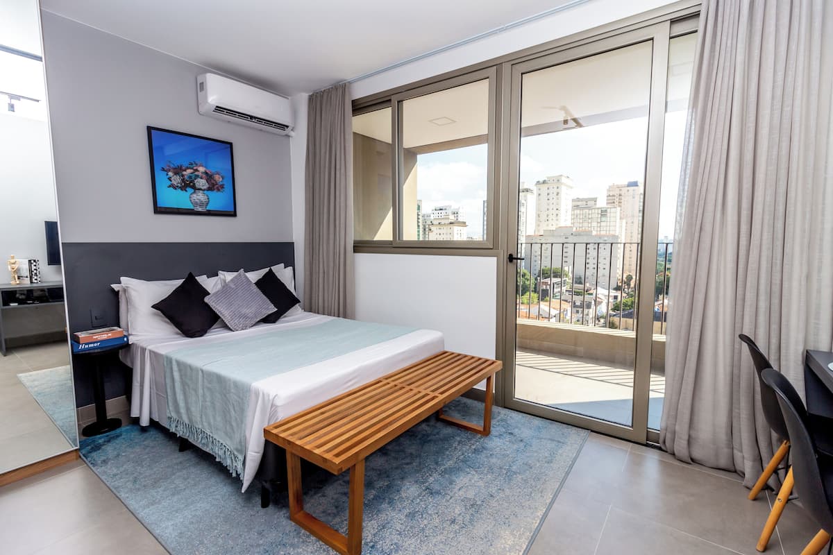 Ein modernes Hotelzimmer mit einem Bett, Nachttisch und Blick auf die Stadt durch große Fenster.