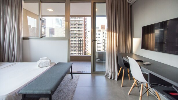 A hotel room with a bed, a desk, a chair, a TV, and a balcony with a city view.