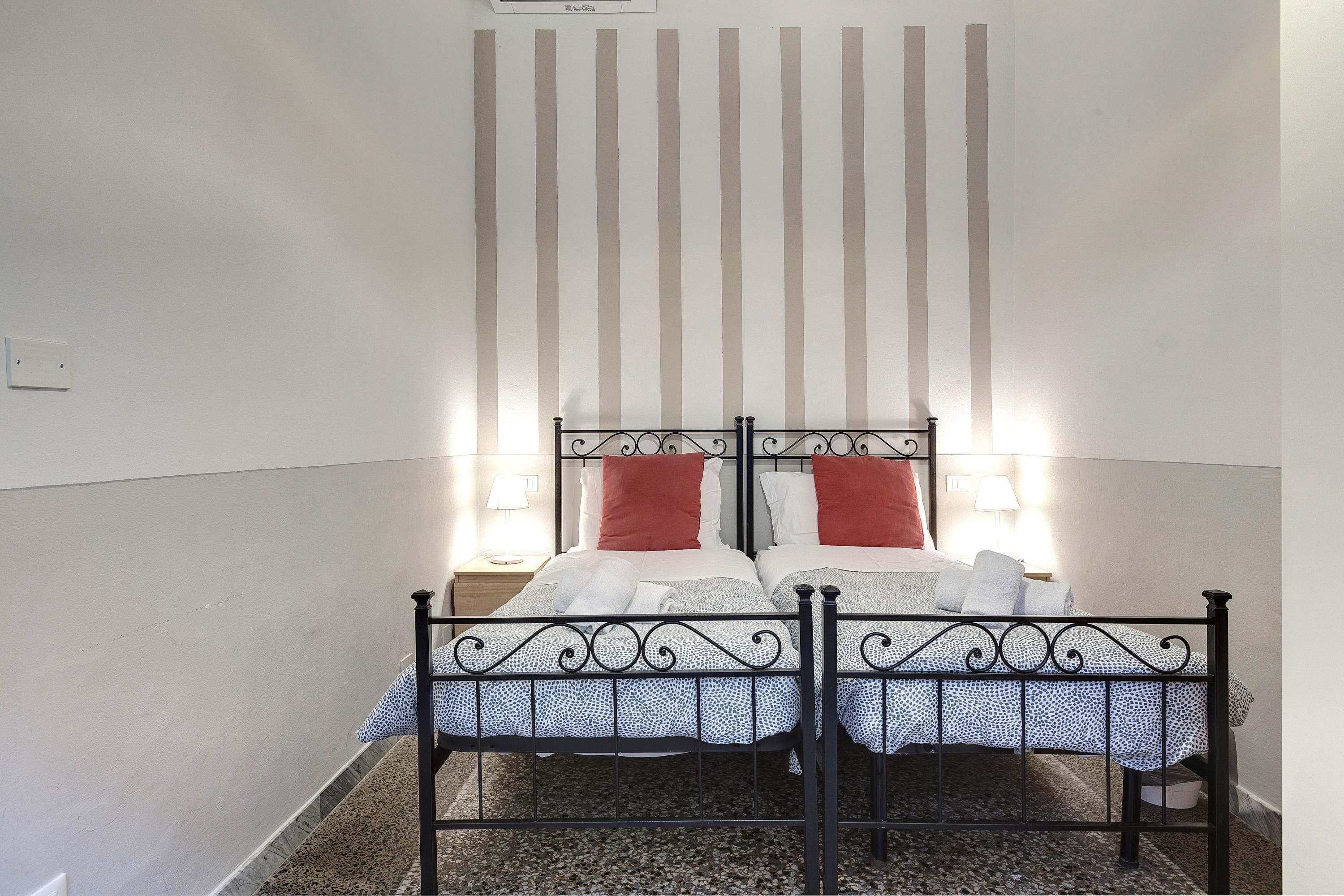 Ein Einzelbett mit Metallgestell, zwei Kissen und einer gemusterten Tagesdecke.