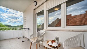 A balcony with two white chairs, a small round table with a tray of items, and a view of a red-tiled roof and greenery. - A2- Luxury apt w big Balcony, 4 min Walk to Beach (Split)