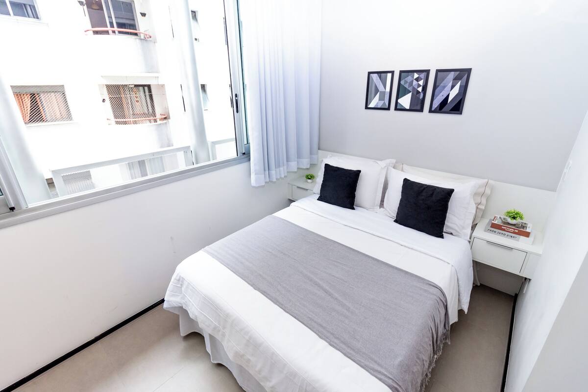 A neatly arranged bedroom with a bed, white nightstands, and a window with curtains.