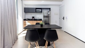Una cocina moderna con microondas integrado, refrigerador y cafetera. Hay una mesa de comedor con cuatro sillas y una planta pequeña encima.
