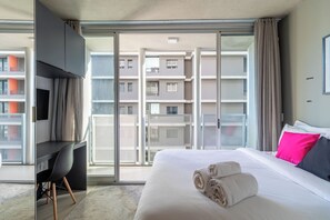 A hotel room with a bed, a desk, a chair, and a large window offering a view of other buildings. - 360 VN Frei Caneca by Housi (São Paulo)