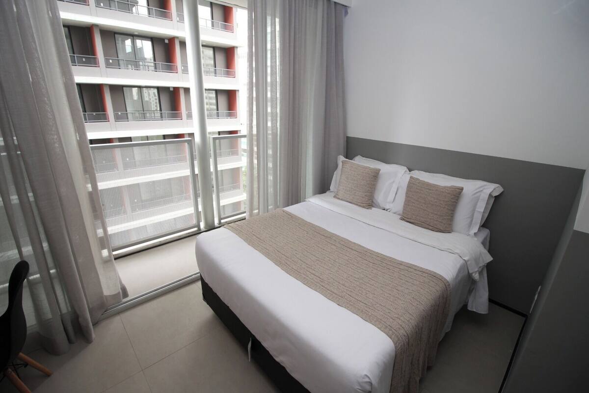 A hotel room with a bed, a chair, and a view of a building through a window.