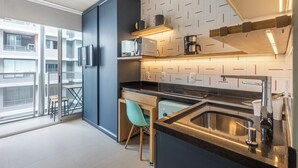 Una cocina moderna con horno integrado, cafetera y pileta. Se ve una ventana con vista a un edificio.