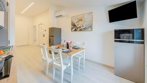 Una cocina moderna con zona de comedor, sillas blancas, una mesa con un florero y un televisor montado.