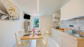Una cocina moderna con zona de comedor, armarios de madera, horno empotrado y ventana con vistas al verdor.