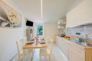 Una cocina moderna con zona de comedor, armarios de madera, horno empotrado y ventana con vistas al verdor.