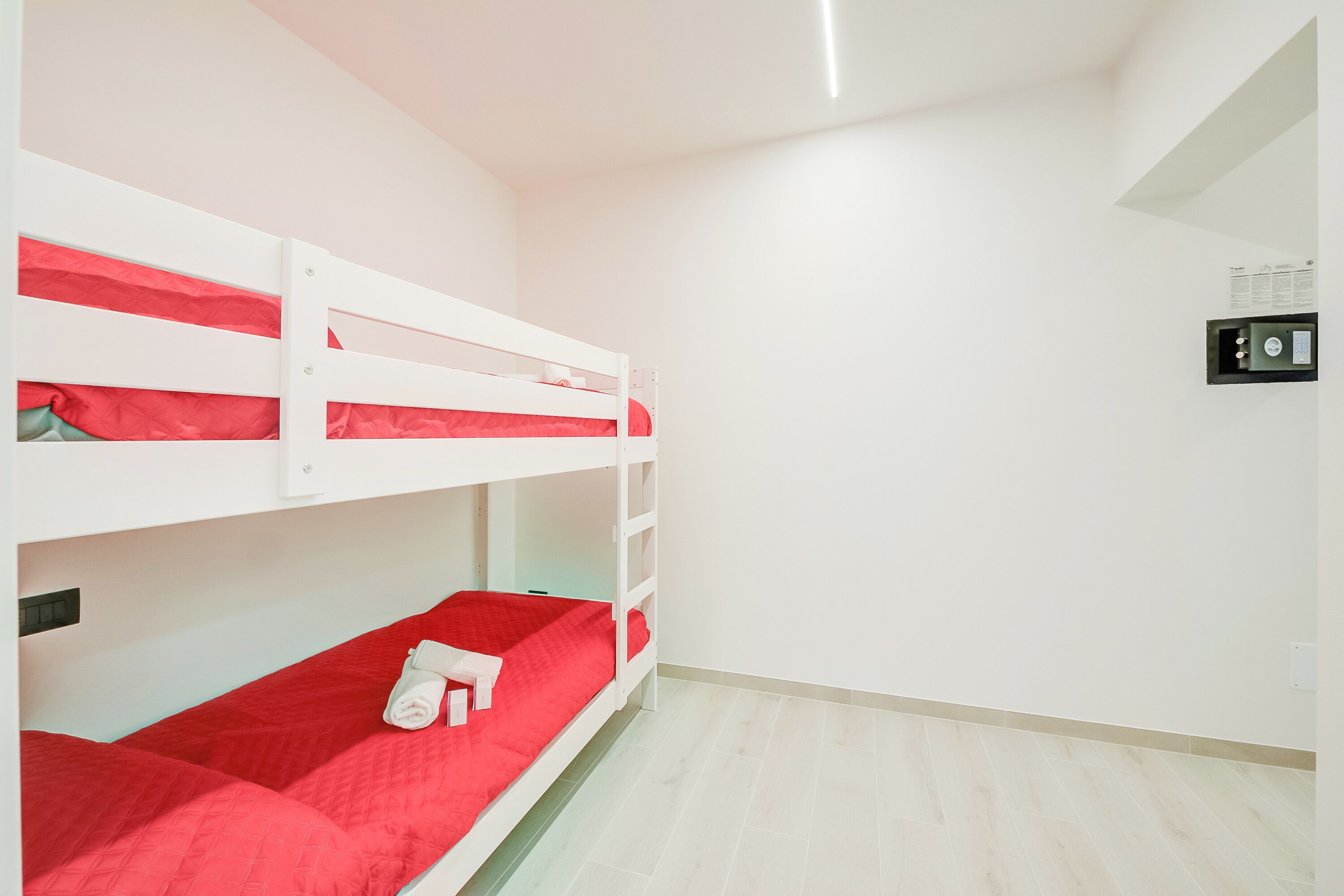Une chambre avec un lit superposé, une couette rouge, un mur blanc et un interrupteur.