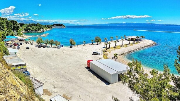 Uma área costeira com estacionamento, um edifício e vista para o mar e montanhas.