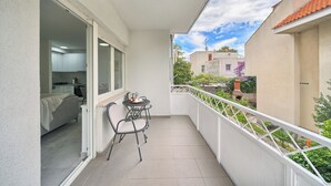 Varanda com mesa e cadeiras, vista para edifícios vizinhos e guarda-corpo branco.