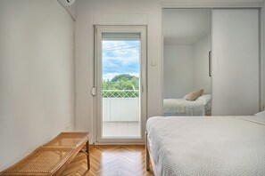 A bedroom with a bed, a bench, a sliding door to a balcony, and a wardrobe.