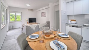 Uma sala de estar moderna com área de jantar, cozinha e televisão ao fundo.