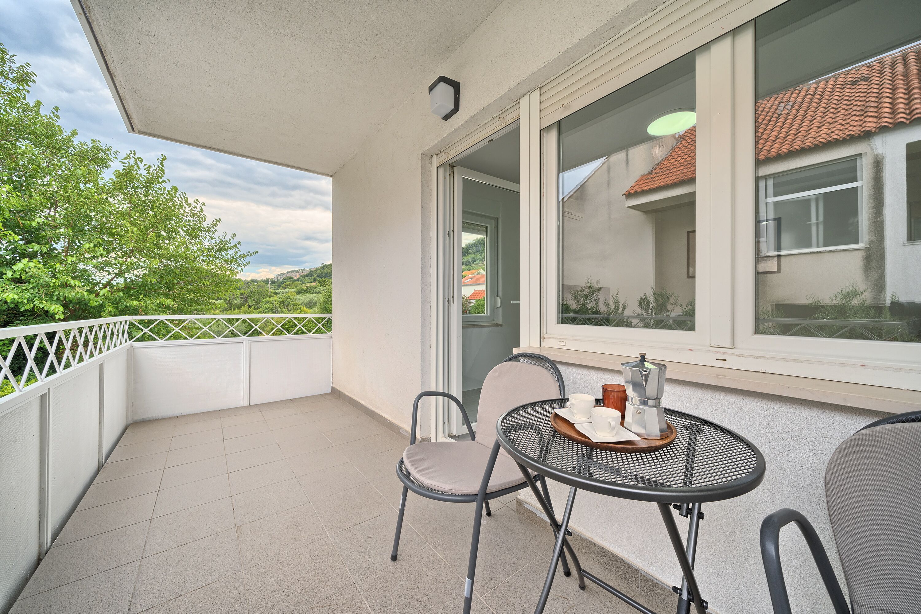A balcony with a table and chairs, a view of a house, and a white railing.