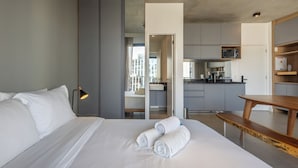 A modern hotel room with a bed, a bedside lamp, a wooden bench, and a view of the city through a large window. - 360 VN Faria Lima (São Paulo)