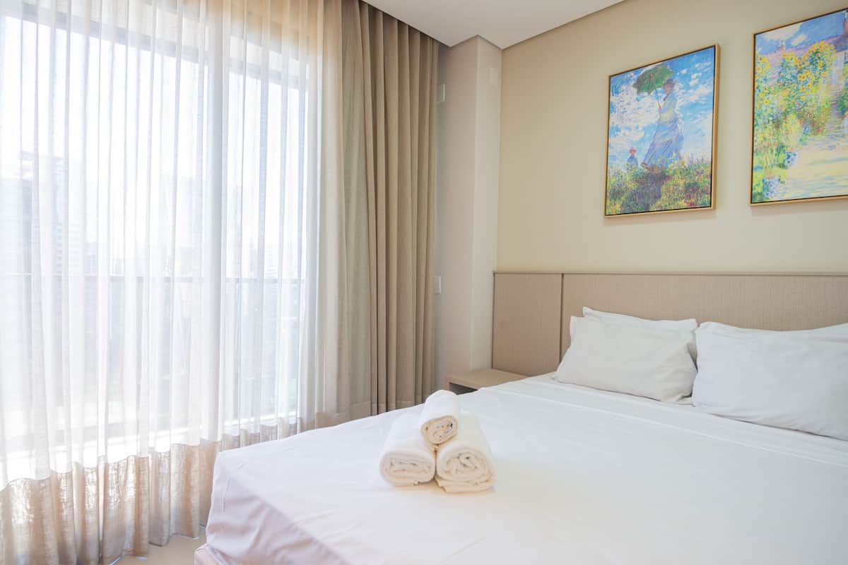 Habitación de hotel con una cama grande, una mesita de noche y una ventana con cortinas translúcidas.