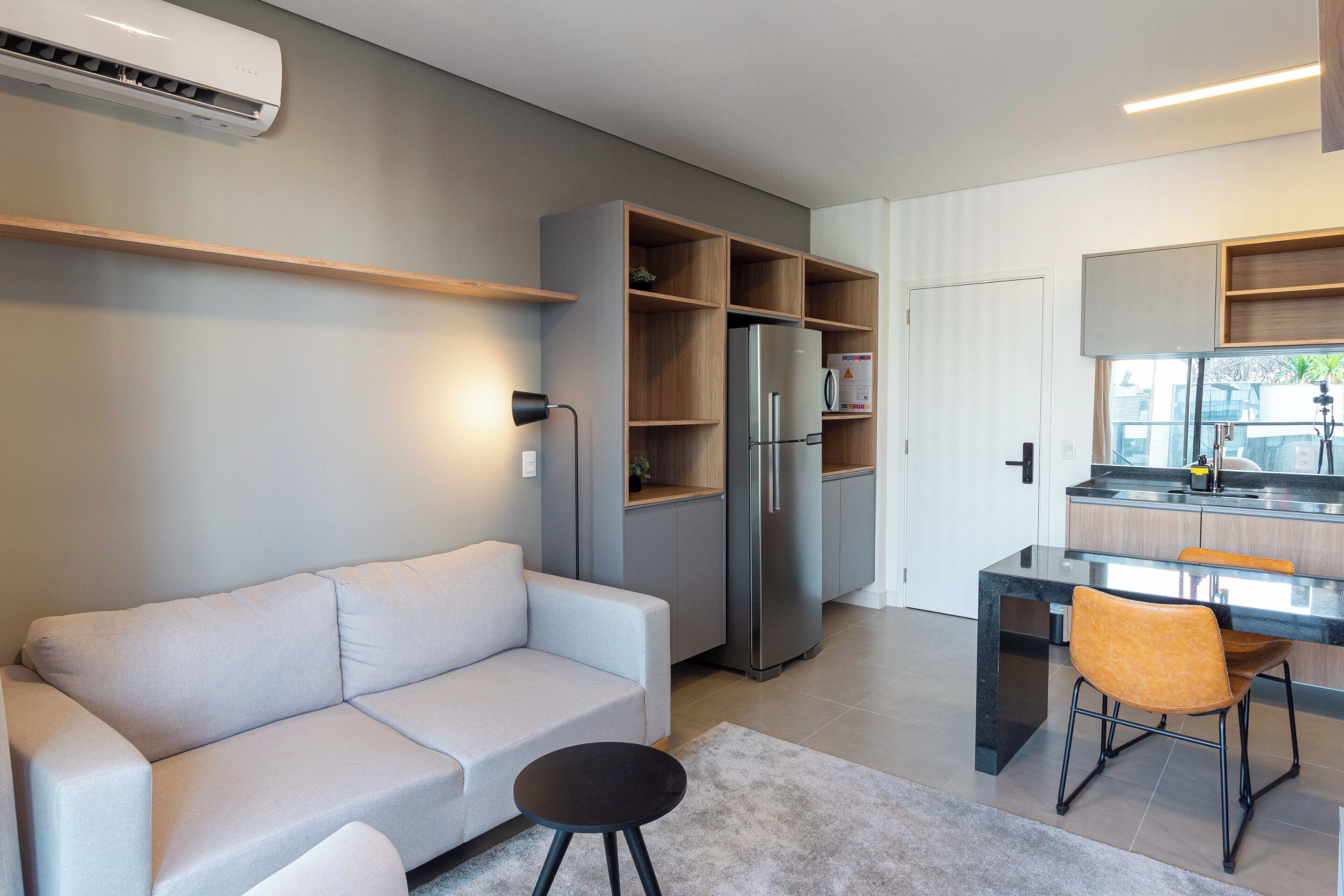 Una cocina moderna con electrodomésticos integrados, un sofá gris y un comedor con una mesa pequeña y sillas.
