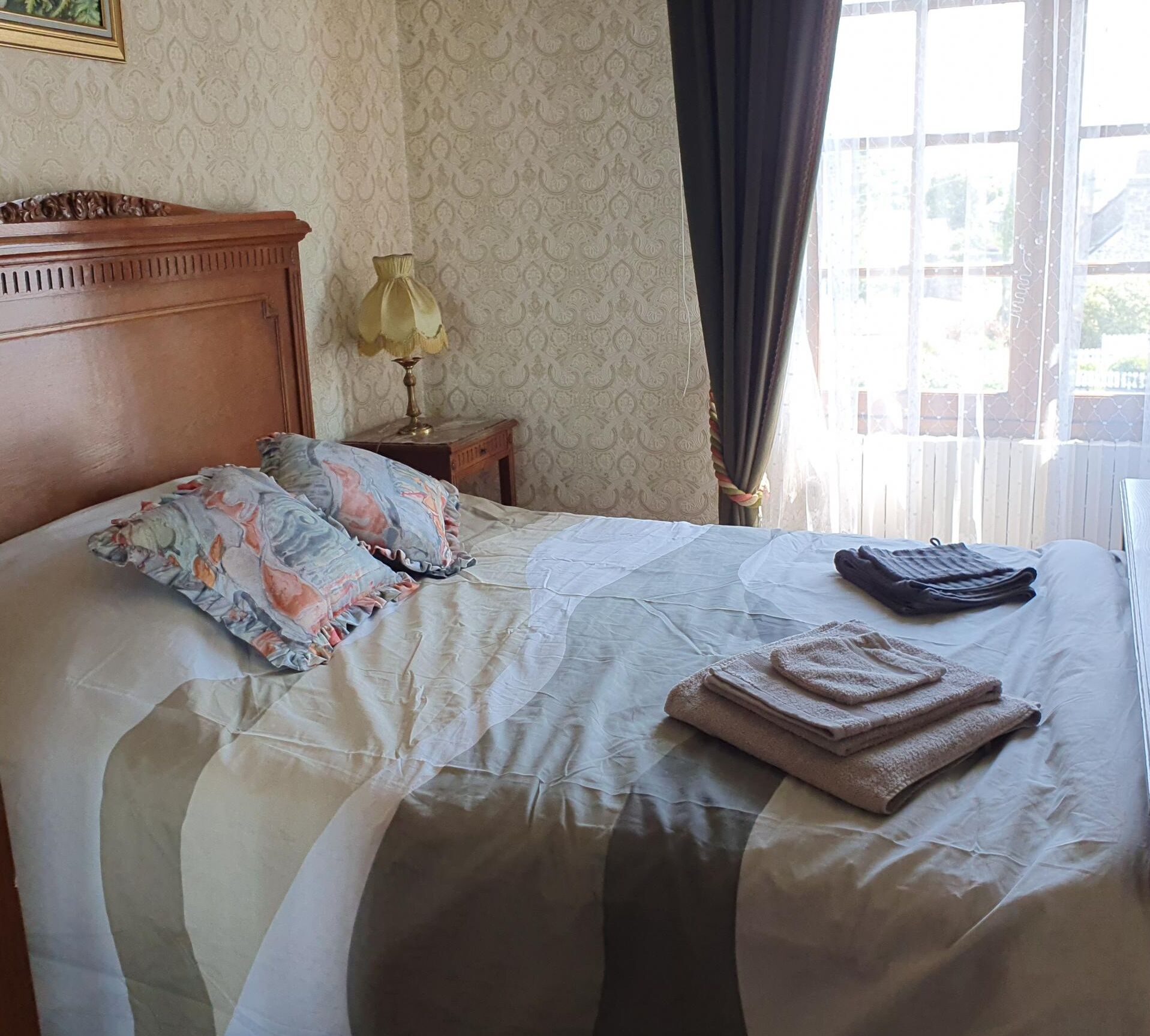 Una cama bien hecha con un cojín estampado, una lámpara de noche y toallas dobladas sobre la cama de una habitación de hotel.