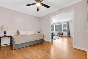 Une chambre à coucher avec un lit, deux tables de chevet avec des lampes, un ventilateur de plafond et une vue sur un balcon équipé d’une chaise et d’une table.