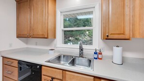 A kitchen with wooden cabinets, a double sink, a window with a view of greenery, and a dishwashing unit. - Fantastic for Extended Stays & Work Crews- 10 beds, 5 bedrooms, 2.5 baths (Warner Robins)
