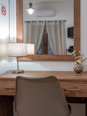 A wooden desk with a lamp, a mirror, and a vase with flowers.