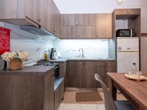A compact kitchen with wooden cabinets, a built-in microwave, and a small dining area. - Atalanti Seaside Junior Suites (Viannos)