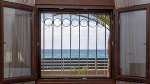 A room with a bed, a window with curtains, and a view of the sea. - Atalanti Seaside Junior Suites (Viannos)