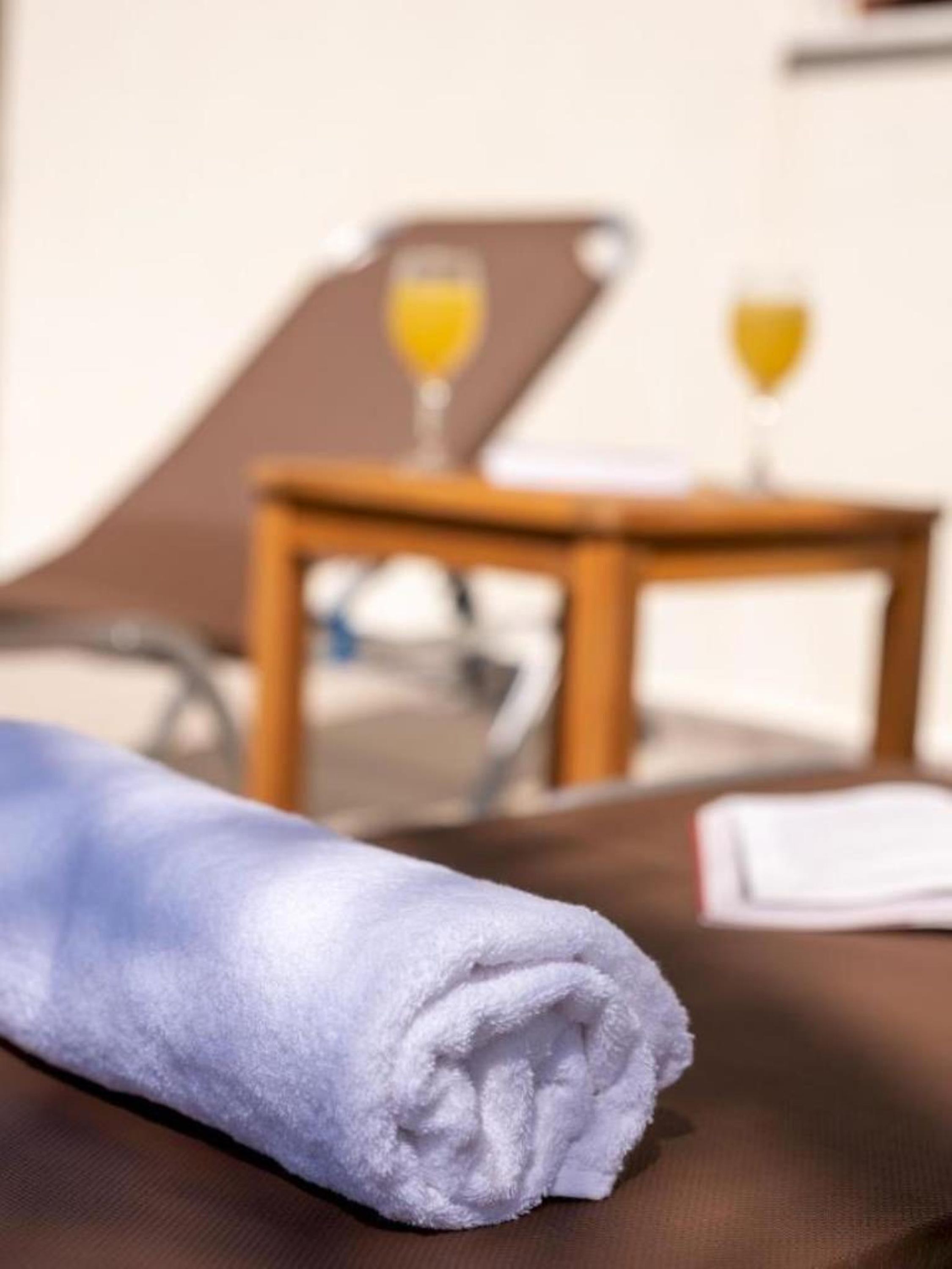 A neatly folded towel on a brown chair, a small wooden table with two glasses of orange juice, and a white notepad.