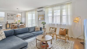 A modern living room with a blue sofa, a round coffee table, and a dining area with a table and chairs.