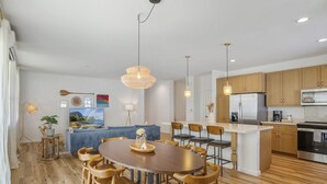 A modern kitchen with wooden cabinets, a central island, and a dining area with a round table and chairs.