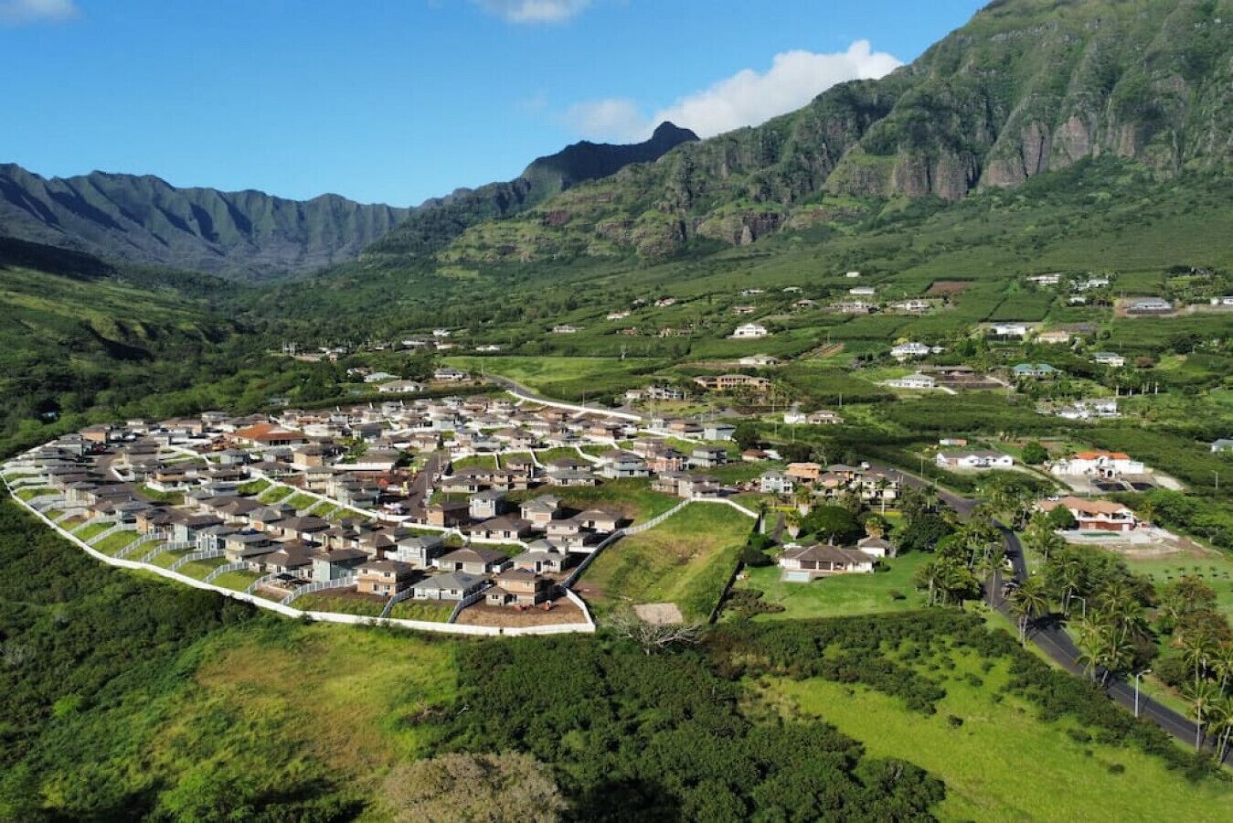 Luchtbeeld van een woongebied met huizen in een cirkelvormig patroon, omringd door weelderige groene heuvels en bergen.